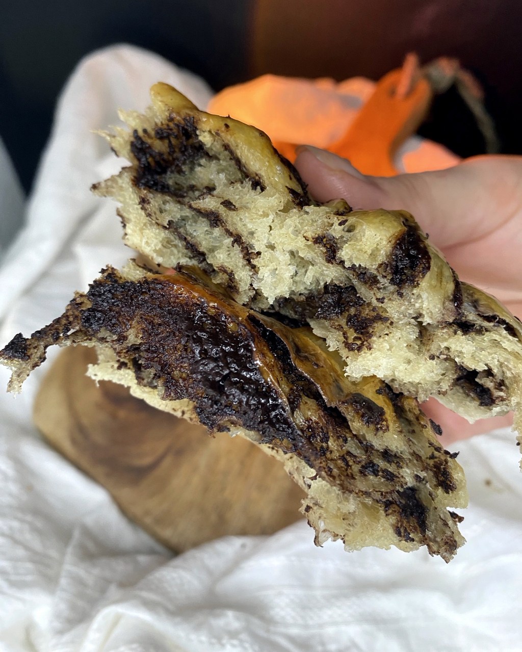 A chocolate bun pulled apart by hand, showing the soft crumb and dark chocolate swirl inside.